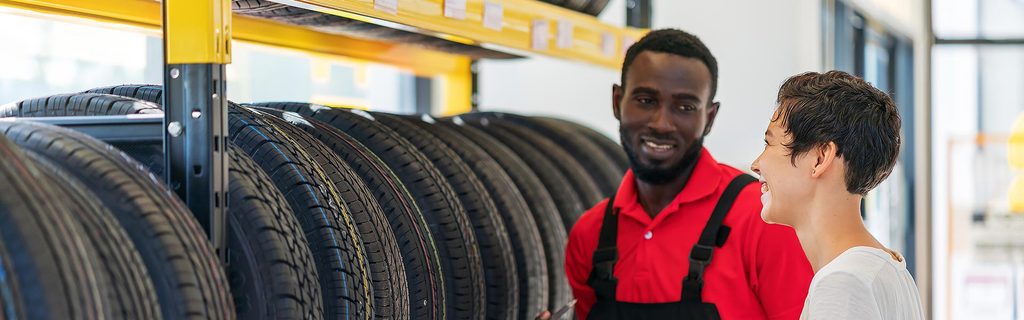 Customer speaking with an automotive service technician beside a display of tires in a dealership service center