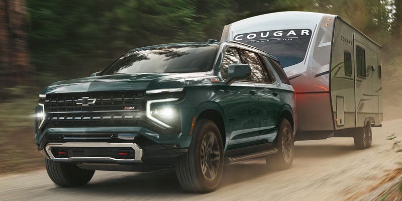 Dark green Chevrolet Tahoe towing a travel trailer along a forest dirt road.