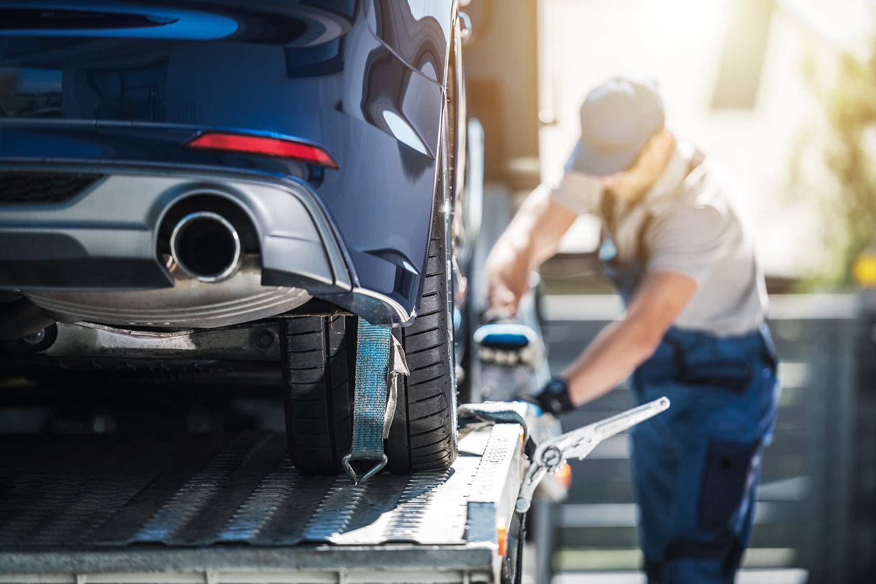 Technician securing a blue car to a tow truck’s loading platform.